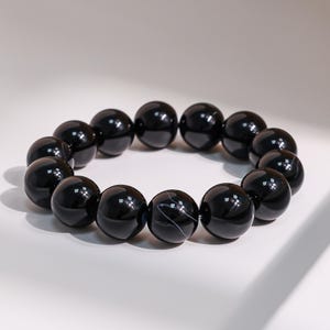 May include: A black beaded bracelet. The bracelet is made of large, round, polished black beads. One bead has a white stripe. The beads are strung together to form a circular shape.