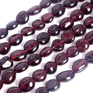 May include: Five strands of polished, deep red garnet beads arranged in parallel rows. Each strand consists of smooth, oval-shaped stones with a glossy finish, strung together on a thin, dark red cord, showcasing natural variations in color.