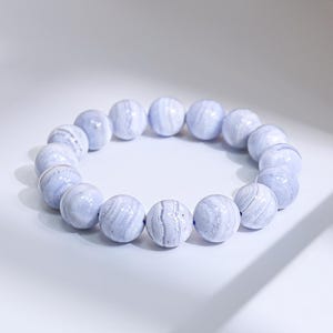 May include: A light blue beaded bracelet. The bracelet features large, round beads with a marbled appearance. The beads are strung together to form a circular shape. The bracelet is set against a white background.