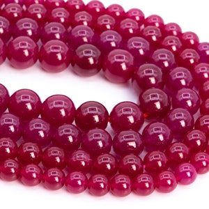 Puede incluir: Una hebra de cuentas redondas de piedras preciosas rosas. Las cuentas son lisas y pulidas, con un acabado brillante.