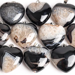 May include: A selection of heart-shaped pendants. The pendants display a variety of black, white, and grey agate stone patterns. Each pendant has a silver-coloured bail for attaching to a chain or cord. The polished stones have a glossy finish.