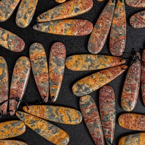 May include: A collection of colorful, teardrop-shaped, polished stones with a variety of brown, orange, and gray patterns. The stones are arranged on a black surface.