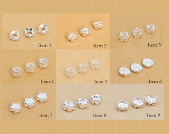 May include: Nine different styles of silver spacer beads for jewellery making. The beads are all silver and have different designs, including flowers, stars, and swirls.