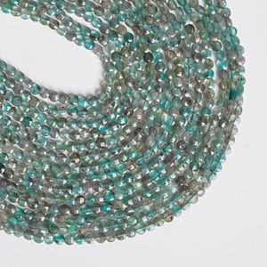 May include: A strand of teal and gray gemstone beads. The beads are round and have a faceted finish. The strand is approximately 18 inches long.