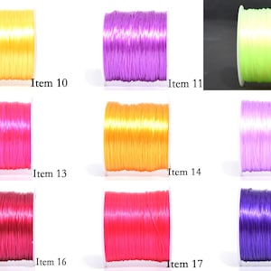 May include: A collection of colorful elastic string spools in various shades, including yellow, purple, green, pink, orange, and red. Each spool is labeled with an item number, offering a range of options for crafting and jewelry making.
