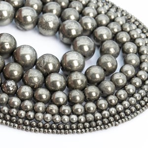 Puede incluir: Una colección de cuentas redondas de pirita metálica de varios tamaños. Las cuentas están dispuestas en un patrón circular, con las cuentas más grandes en el centro y las cuentas más pequeñas en el exterior.