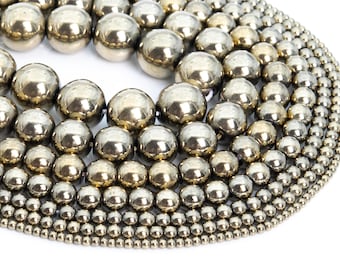 May include: A collection of round, metallic beads in various sizes, arranged in a circular pattern. The beads are a silvery-gold color and have a smooth, shiny finish.