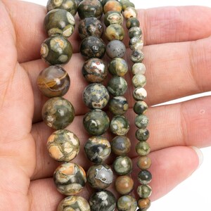 May include: A strand of green, brown, and white gemstone beads. The beads are round and have a speckled pattern. The beads are strung on a clear elastic cord.