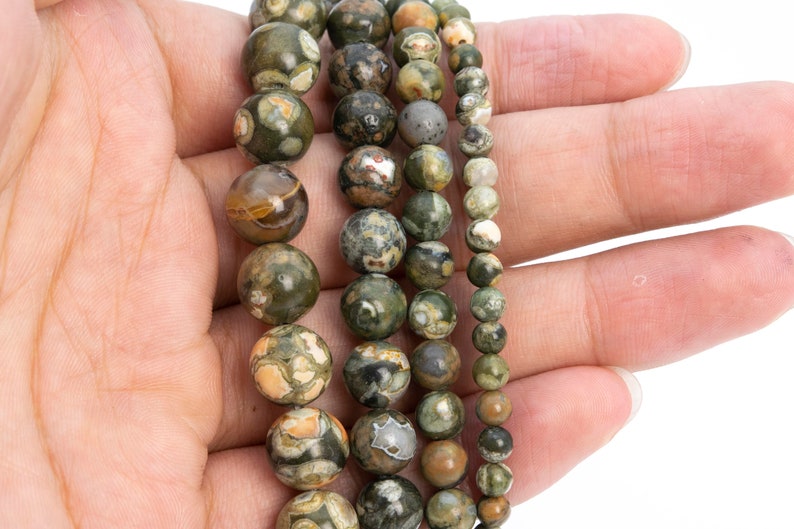 May include: A strand of green, brown, and white gemstone beads. The beads are round and have a speckled pattern. The beads are strung on a clear elastic cord.