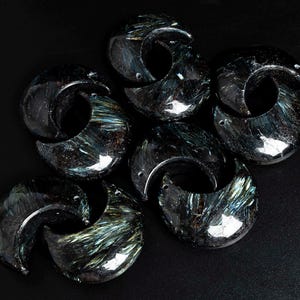 May include: A group of six crescent-shaped, dark blue and green gemstone pendants with a shimmery, iridescent finish.