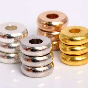 May include: Four stacks of round metal beads in silver, gold, and rose gold. Each stack is made up of four beads.