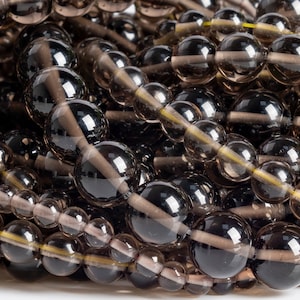 May include: A close-up of a pile of dark brown smoky quartz beads. The beads are round and have a smooth, polished finish. They are strung together on a clear thread.
