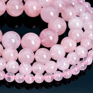 May include: A strand of pink rose quartz beads. The beads are round and smooth, and they are arranged in a circular pattern. The beads are all different sizes, and they are all a light pink color.