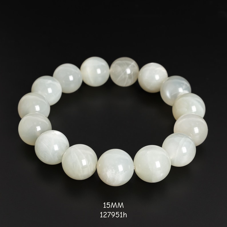 May include: A white beaded bracelet with large, round beads. The beads are a milky white color and appear to have a subtle shimmer. The bracelet is displayed against a black background. Text at the bottom reads "15MM" and "127951h".