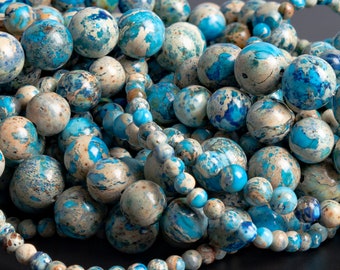 Könnte beinhalten: Nahaufnahme eines Stapels blauer und weißer Jaspisperlen. Die Perlen sind rund und haben eine marmorierte Optik. Sie eignen sich perfekt für die Herstellung von Schmuck oder anderen Bastelarbeiten.