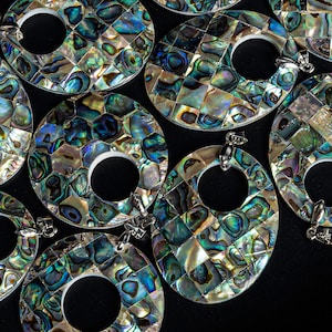 May include: A group of oval-shaped pendants made of iridescent abalone shell. Each pendant has a circular opening in the center and a silver bail for hanging.