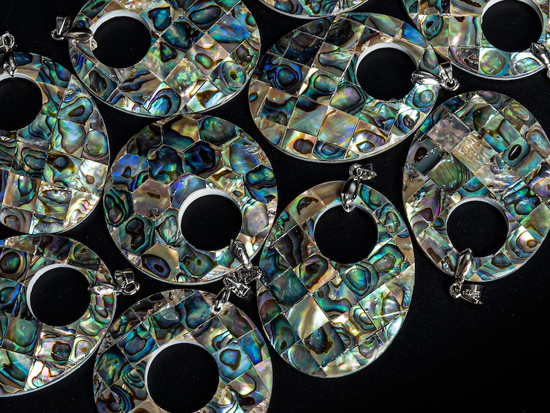 May include: A group of oval-shaped pendants made of iridescent abalone shell. Each pendant has a circular opening in the center and a silver bail for hanging.
