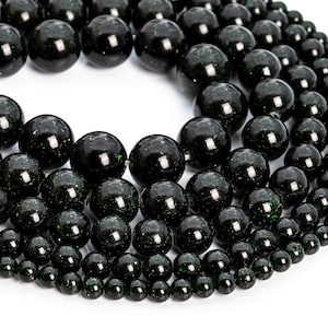 May include: A close-up of a strand of black and green gemstone beads. The beads are round and have a speckled appearance. The beads are arranged in a circular pattern, with the largest beads in the center and the smallest beads on the outside.
