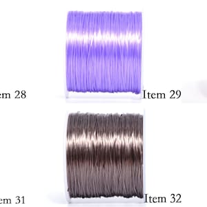 May include: Five spools of colorful elastic cord in pink, purple, orange, red, and gray. Each spool is labeled with an item number. The cords are tightly wound on clear plastic spools, ready for crafting or jewelry making.