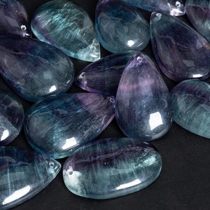 May include: A collection of teardrop-shaped fluorite stones in shades of blue, green, and purple. The stones are smooth and polished, with a glossy finish.