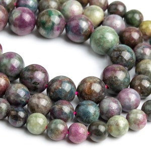May include: A strand of round, multi-colored gemstone beads. The beads are a mix of green, blue, purple, and brown. The beads are strung on a thin, red thread.