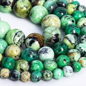 May include: A strand of green and black gemstone beads. The beads are round and have a mottled appearance.