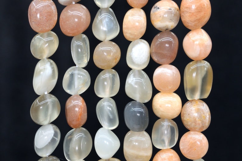 May include: A strand of smooth, oval-shaped sunstone beads in shades of peach, white, and light orange. The beads have a translucent quality and show a shimmery effect.