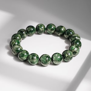 May include: A circular bracelet composed of polished, spherical beads in varying shades of deep forest green and emerald. Each bead features a unique, marbled texture with natural inclusions and a glossy finish, strung together in a continuous loop.