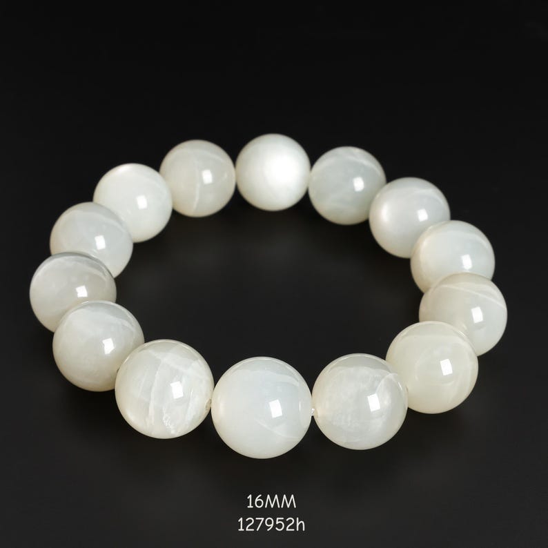 May include: A white beaded bracelet with large, round beads. The bracelet is displayed against a black background. The text "16MM" and "127952h" is at the bottom of the image.