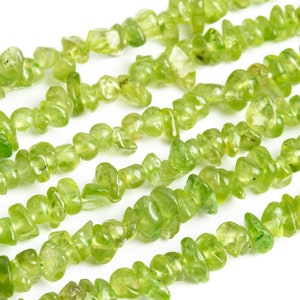 May include: A strand of light green gemstone chips, also known as peridot chips, arranged in a row on a white background.