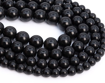 May include: A strand of black gemstone beads, with varying sizes, arranged in a circular pattern. The beads are smooth and polished, with a glossy finish.