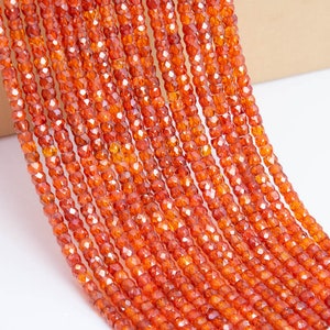 May include: A strand of orange carnelian beads, each bead is faceted and has a slightly irregular shape. The beads are strung on a clear thread and are ready to be used for jewelry making.