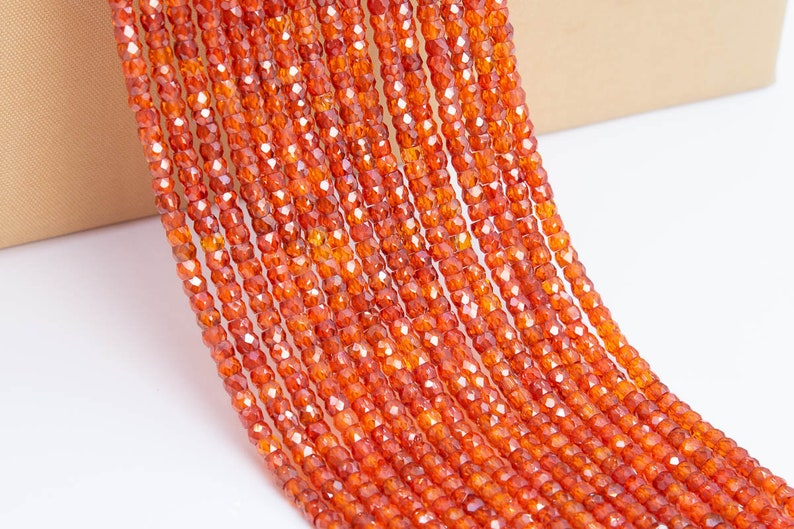May include: A strand of orange carnelian beads, each bead is faceted and has a slightly irregular shape. The beads are strung on a clear thread and are ready to be used for jewelry making.