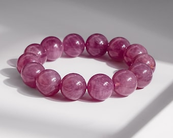 Può includere: Un braccialetto rotondo composto da perline sferiche lucide, rosa-viola. Le perline sono infilate insieme, formando una forma circolare. Il braccialetto è esposto su una superficie bianca con ombre.