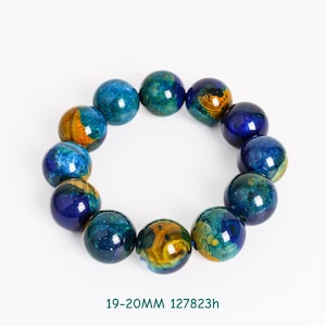 Pu&ograve; includere: Un braccialetto composto da dodici perline sferiche. Le perline sono prevalentemente blu e verdi, con accenti gialli e arancioni. Ogni perlina misura circa 1,9-2,0 cm di diametro. Il testo "19-20MM 127823h" &egrave; in basso.