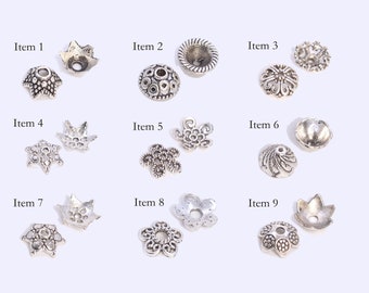 May include: A collection of nine silver-toned metal bead caps in various shapes and designs. The caps include star, floral, and geometric patterns. Each item is labeled with a number from 1 to 9.