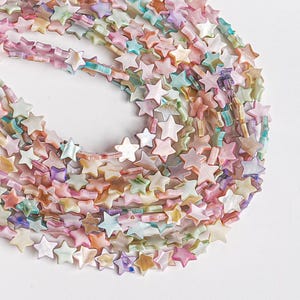 May include: Strands of star-shaped beads in pastel colors, including pink, blue, green, and yellow. The beads have a pearlescent sheen and are strung together, creating a delicate and whimsical appearance. Ideal for jewelry making.