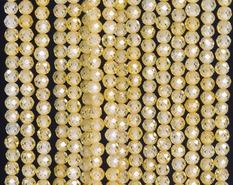 May include: Rows of faceted, yellow crystal beads hang against a black background. The beads are round and have multiple facets that catch the light, creating a sparkling effect. The beads are strung together, forming vertical lines.