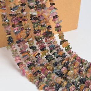 May include: Strands of colorful tourmaline chip beads. The beads display a variety of colors, including pink, green, brown, and black. The chips are irregular in shape and size, creating a natural, organic look. The beads are strung together, ready for jewelry making.