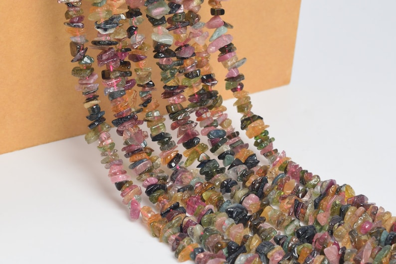 May include: Strands of colorful tourmaline chip beads. The beads display a variety of colors, including pink, green, brown, and black. The chips are irregular in shape and size, creating a natural, organic look. The beads are strung together, ready for jewelry making.