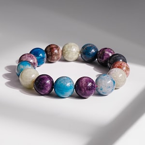 May include: A beaded bracelet featuring a variety of colorful, round gemstones. The bracelet includes stones in shades of blue, purple, brown, and white. The beads are strung together to form a circular shape.