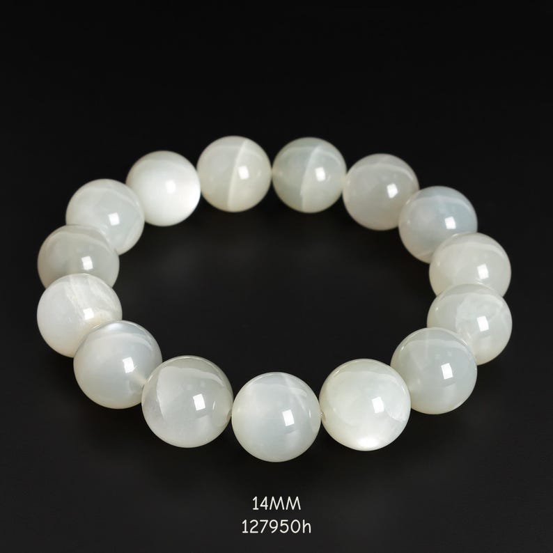 May include: A bracelet featuring large, round, off-white beads. The beads have a pearlescent sheen and are strung together to form a circular shape. The text "14MM" and "127950h" is at the bottom of the image.