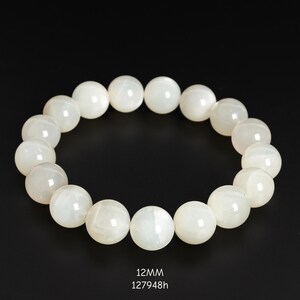 May include: A white beaded bracelet with 12mm beads. The bracelet is made of round, opaque beads with a subtle sheen. The beads are strung together to form a circular shape. The text "12mm" and "127948h" is visible at the bottom.