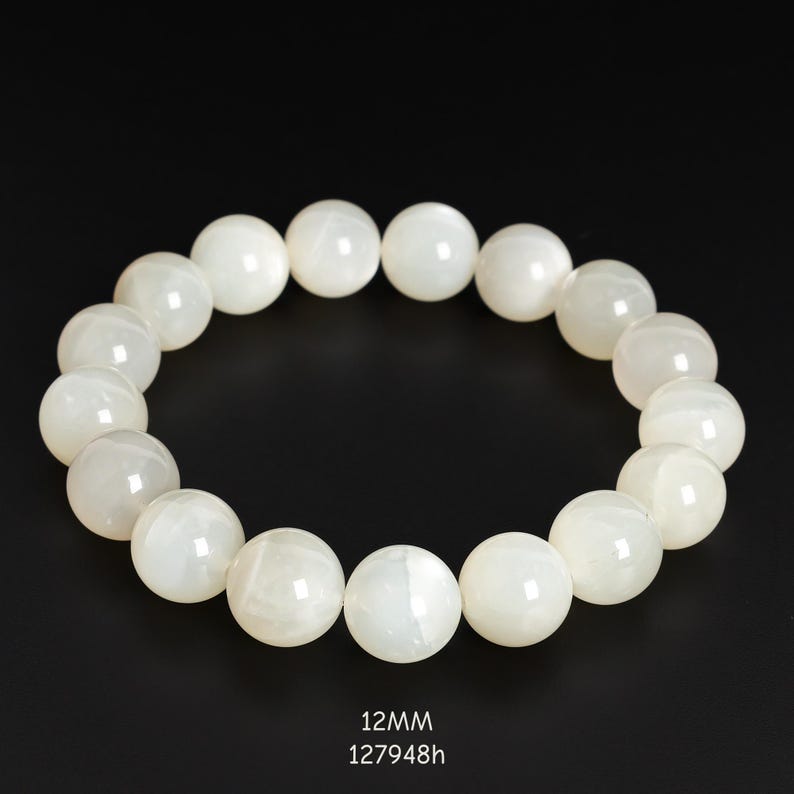 May include: A white beaded bracelet with 12mm beads. The bracelet is made of round, opaque beads with a subtle sheen. The beads are strung together to form a circular shape. The text "12mm" and "127948h" is visible at the bottom.