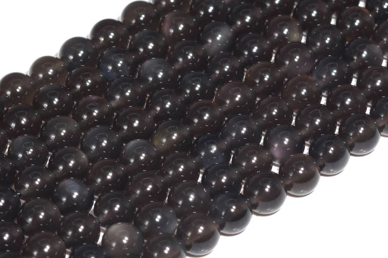 May include: A strand of black gemstone beads with a subtle iridescent sheen. The beads are round and smooth, and they are strung together on a clear thread.