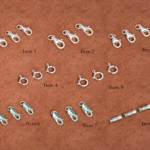May include: Assortment of silver-toned jewelry findings, including lobster clasps, jump rings, and barrel clasps.  The findings are arranged in rows on a brown surface.