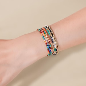 May include: A collection of colorful beaded bracelets. The bracelets feature a variety of colors, including red, orange, turquoise, black, and gold. The bracelets are made of small, round beads strung together.