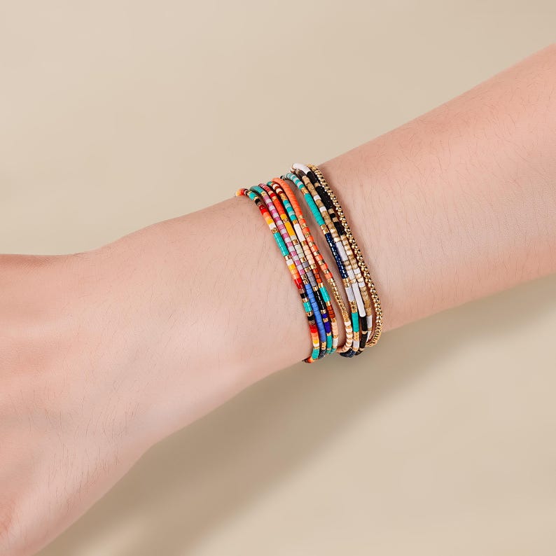 May include: A collection of colorful beaded bracelets. The bracelets feature a variety of colors, including red, orange, turquoise, black, and gold. The bracelets are made of small, round beads strung together.