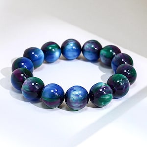 May include: A stretch bracelet composed of fourteen spherical beads. Each bead features a swirling, marbled pattern of deep blue, vibrant green, and dark purple hues with a glossy, reflective finish, arranged in a circular loop on a white surface.