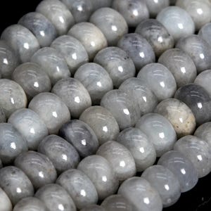 May include: Close-up of a strand of smooth, oval-shaped beads. The beads are a mix of pale gray and white, with a glossy finish. The beads are strung together, creating a pattern of light and shadow.